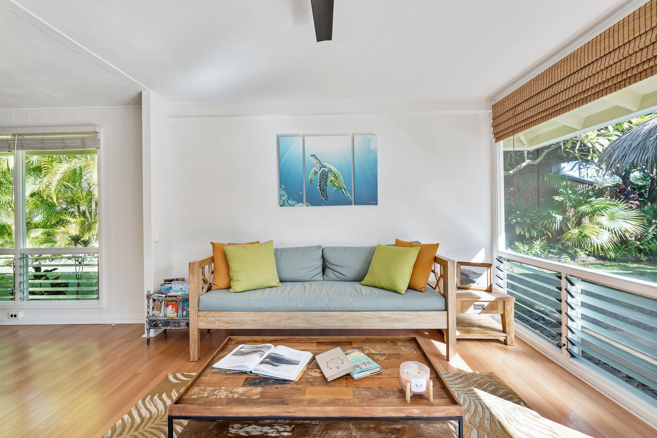 Bright tropical living room with wood sofa, green and yellow pillows, turtle wall art, and large windows