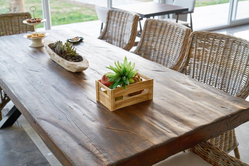 Wooden dining table with wicker chairs, potted plant centerpiece and snacks by window
