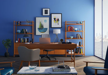 Modern office cubicle with blue walls, wooden desk, bookshelves, and wall art
