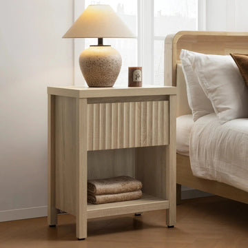 Modern wood nightstand with lamp, candle, and folded towels beside a bed