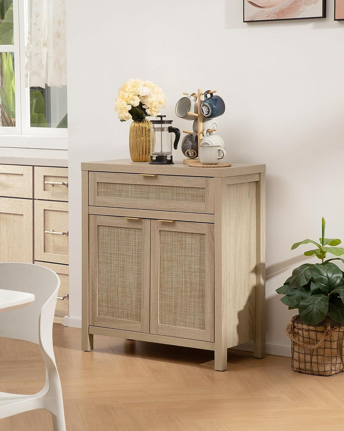 Light wood buffet cabinet with rattan doors, coffee mugs, French press, and vase of flowers