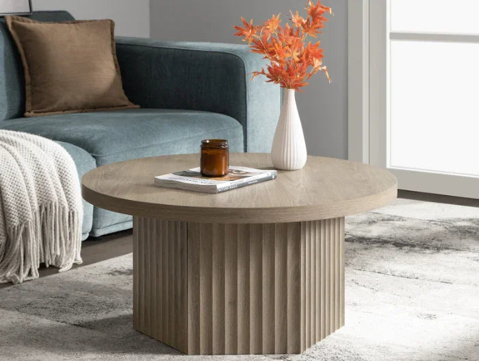 Modern round wood coffee table with vase, autumn leaves, and candle in cozy living room