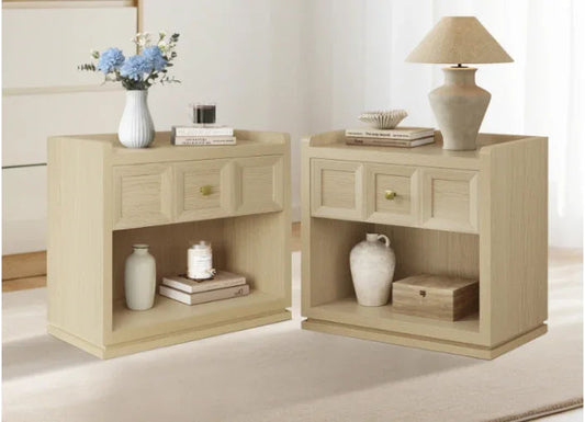 Pair of light wood nightstands with drawers, books, vases, lamp, and flowers in a modern bedroom.