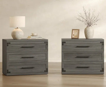 Two gray wooden dressers with black handles, topped with a lamp, books, vase, and framed photo