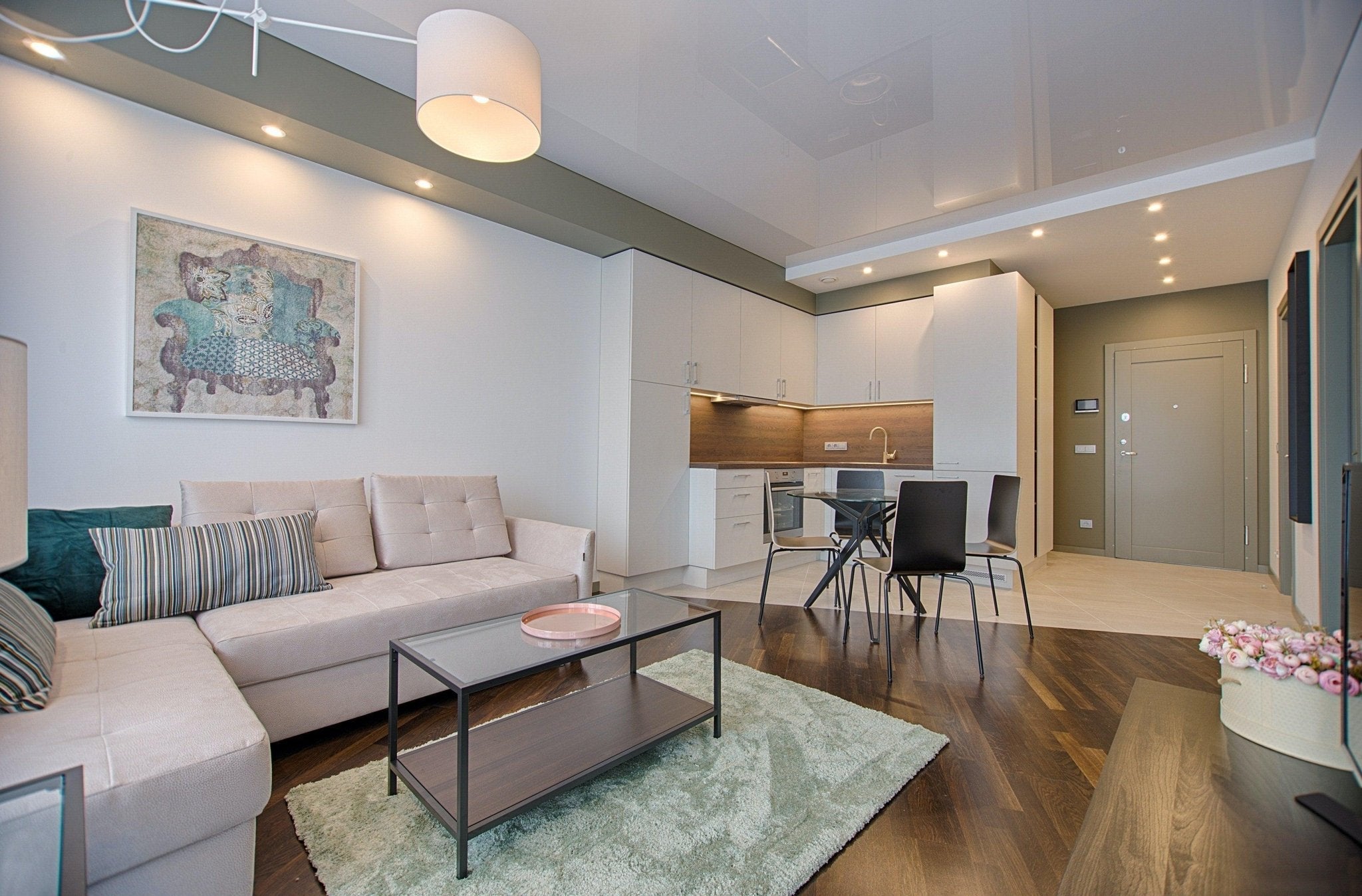 Modern open-plan living room and kitchen with beige sofa, glass coffee table, and wooden floor.