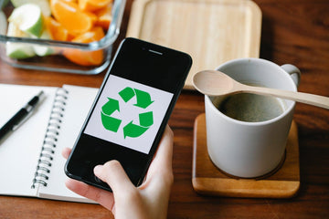 Hand holding phone with green recycle symbol, eco-friendly workspace with coffee and fruit