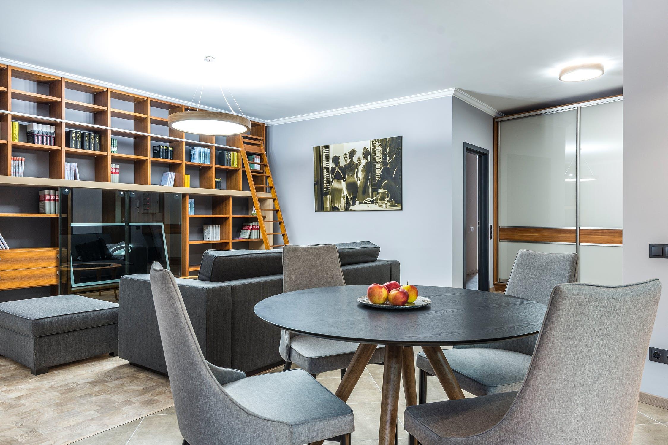 Modern living room with round dining table, gray chairs, wall art, and wood bookshelves