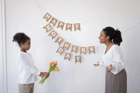 Child giving flowers to mom with Happy Mother's Day banner on white wall