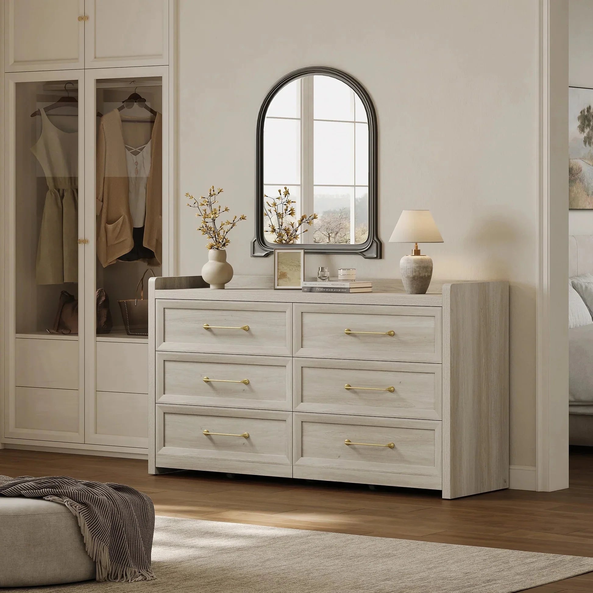 Modern bedroom with light wood dresser, gold handles, arched mirror, lamp, and vase decor
