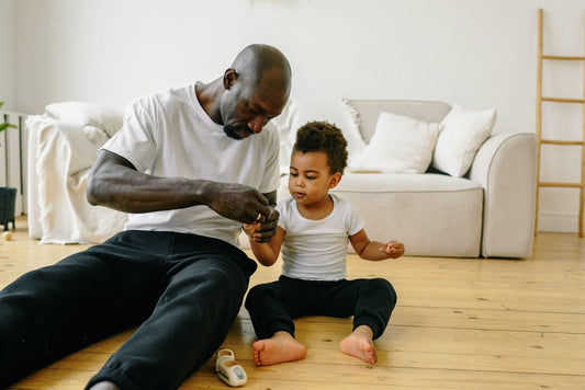 Father and child in matching white shirts sitting on living room floor, cozy sofa behind them