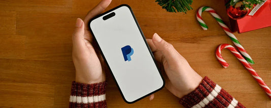 Hands holding a smartphone with PayPal logo, candy canes and gifts on wooden table