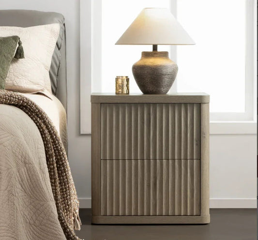 Modern wood nightstand with fluted design, ceramic table lamp, and candle by a bed
