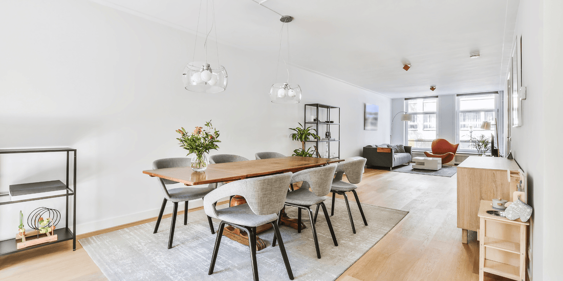 Modern dining room with wooden table, grey chairs, pendant lights, and open living area