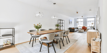 Modern dining room with wooden table, grey chairs, pendant lights, and open living area