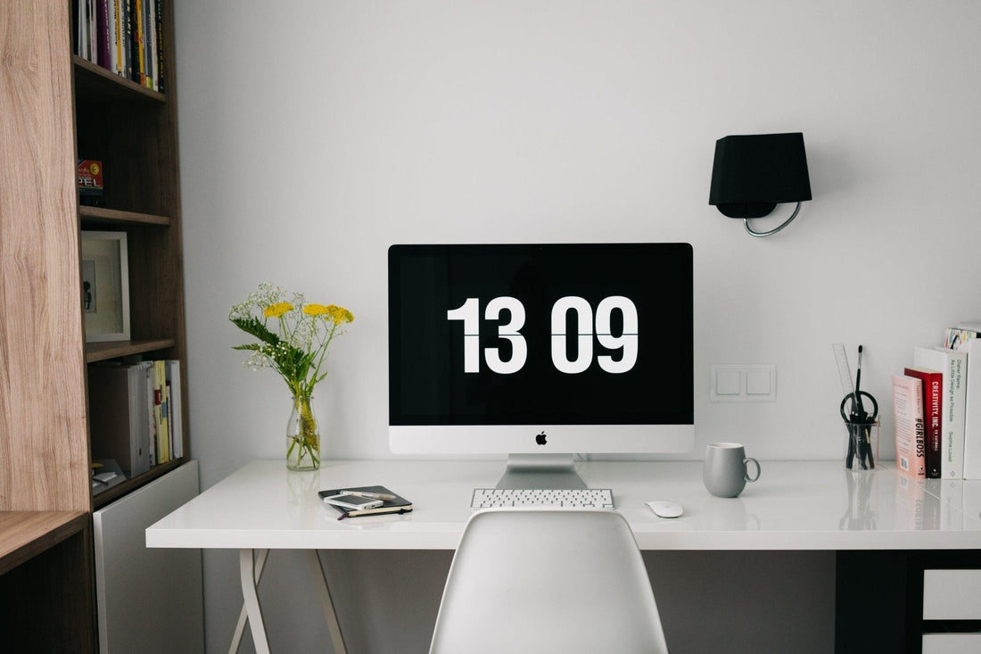 Minimalist home office desk with iMac, digital clock display, and vase of yellow flowers