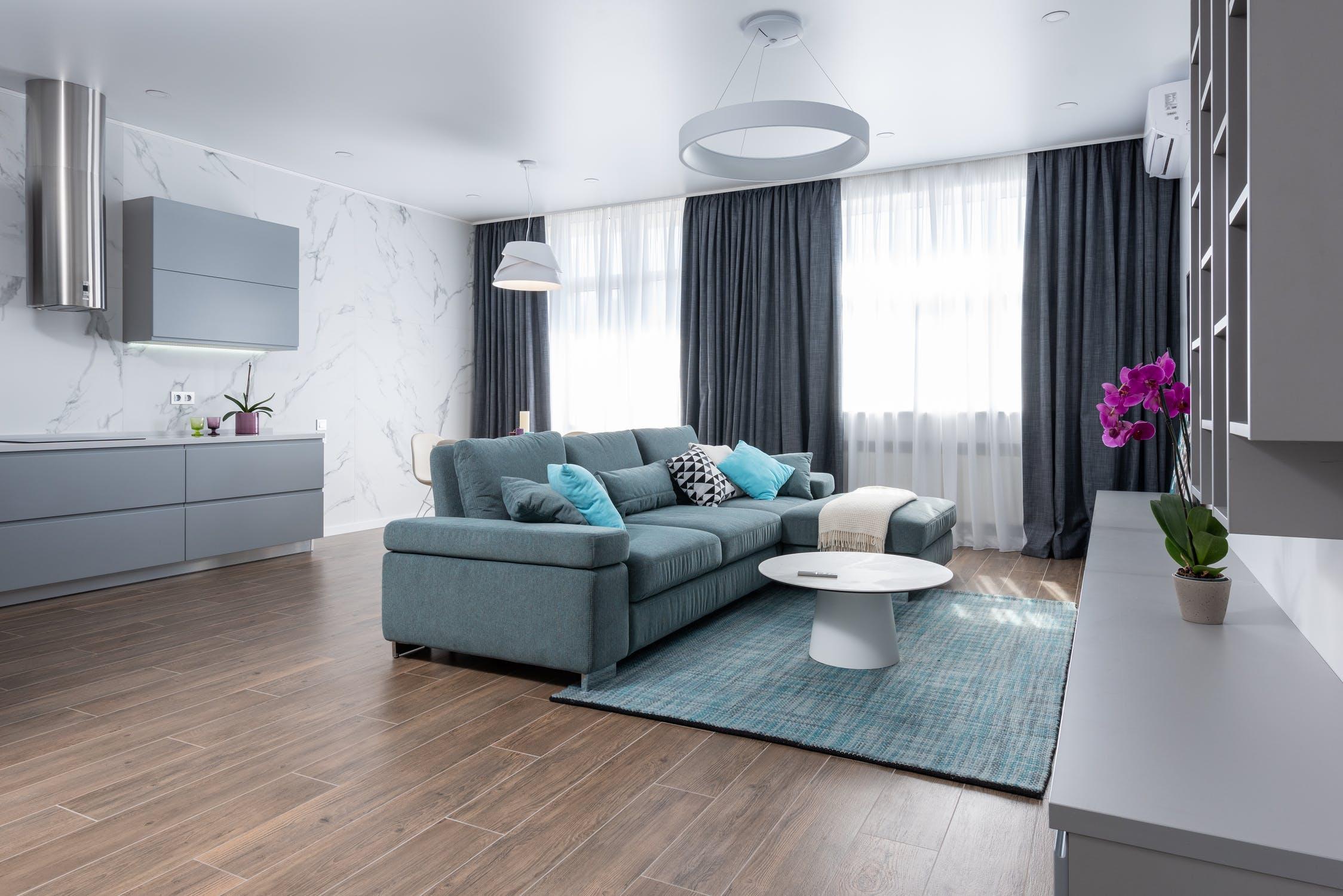 Modern living room with blue sofa, marble wall, wood floor, and orchid on counter