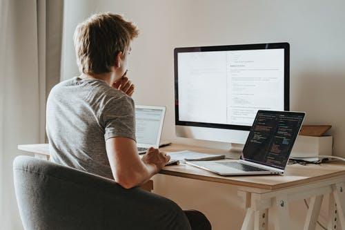 Man working from home at desk with desktop and two laptops, home office setup