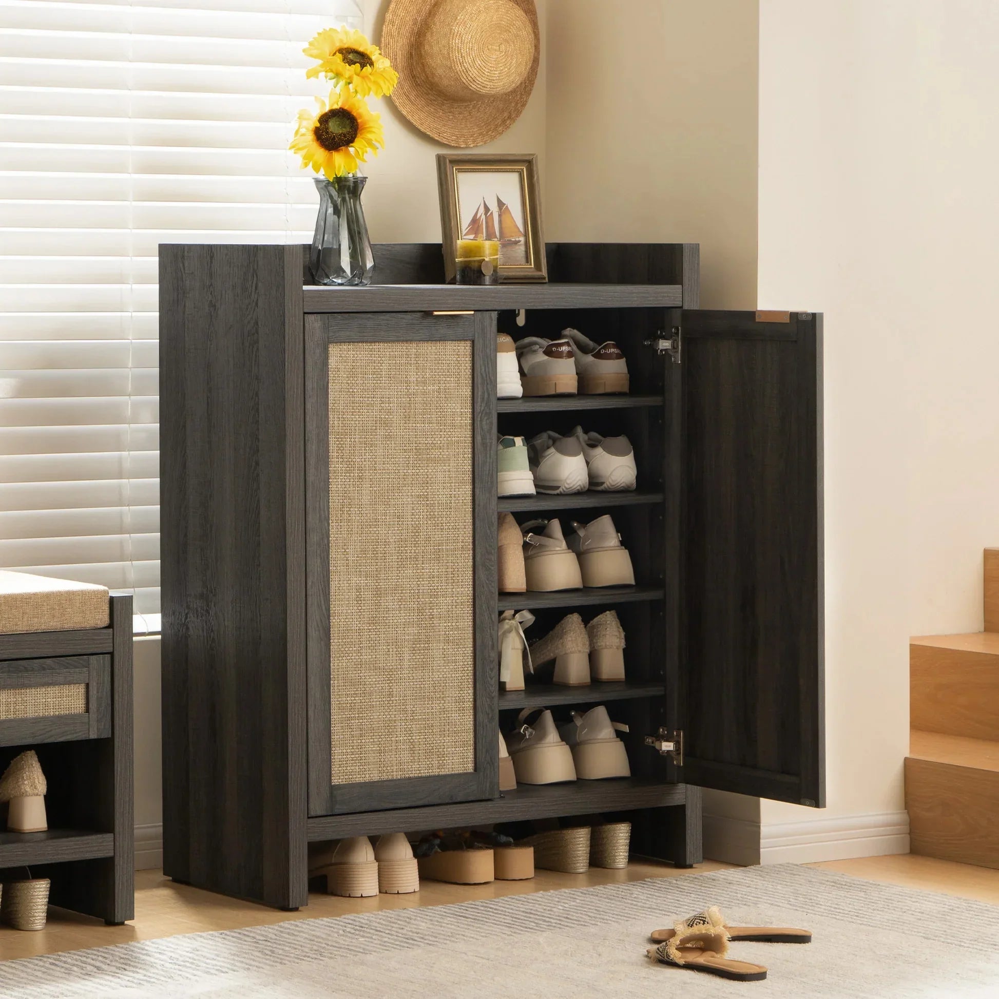 Modern dark wood shoe cabinet with woven rattan doors in entryway, shoes organized inside.