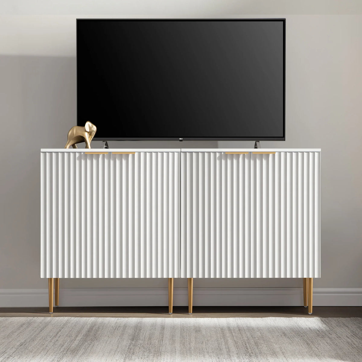 Modern white TV stand with gold legs, flat-screen TV, and gold elephant decor in a minimalist room