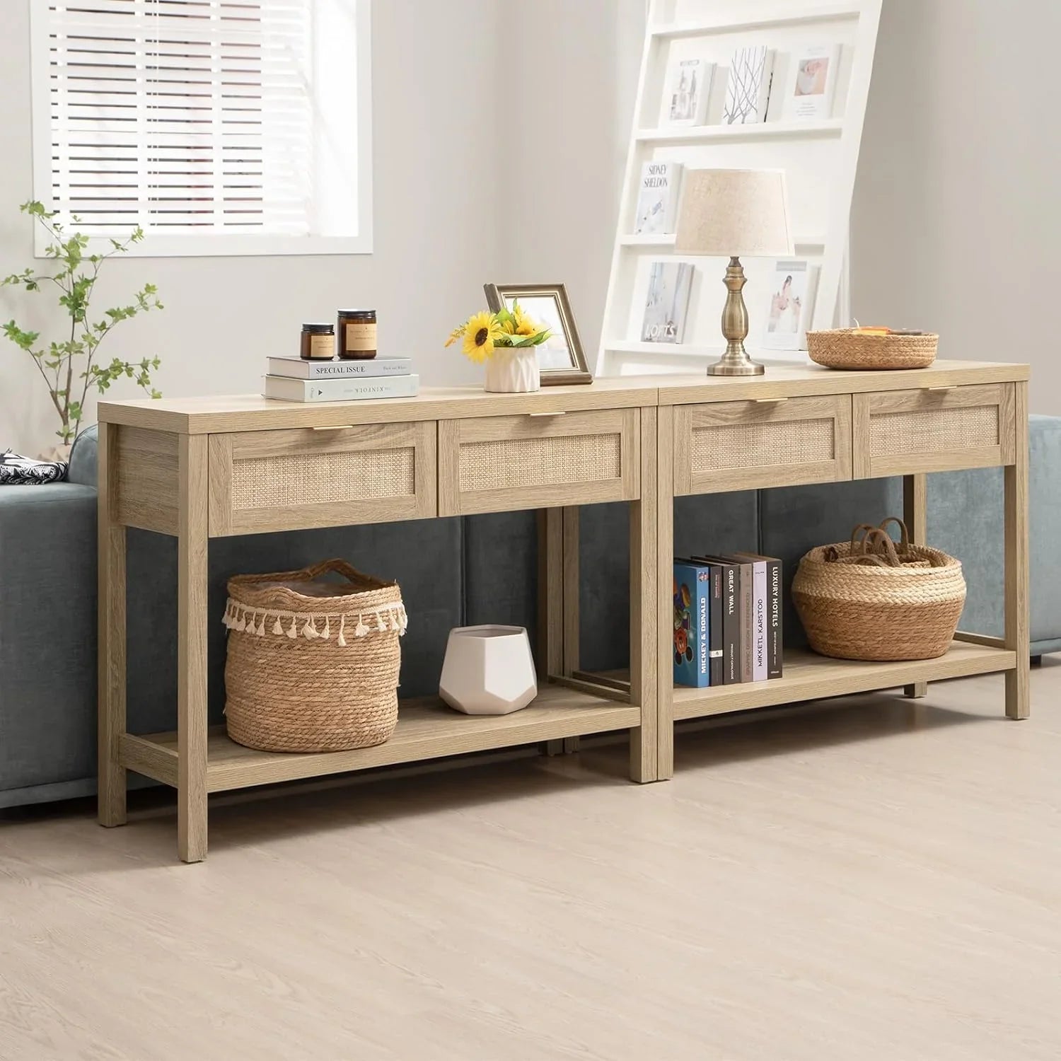 A black wooden console table with woven rattan panels on the drawers, gold handles, and a lower shelf, decorated with a handbag, a vase with flowers, and a lamp.
