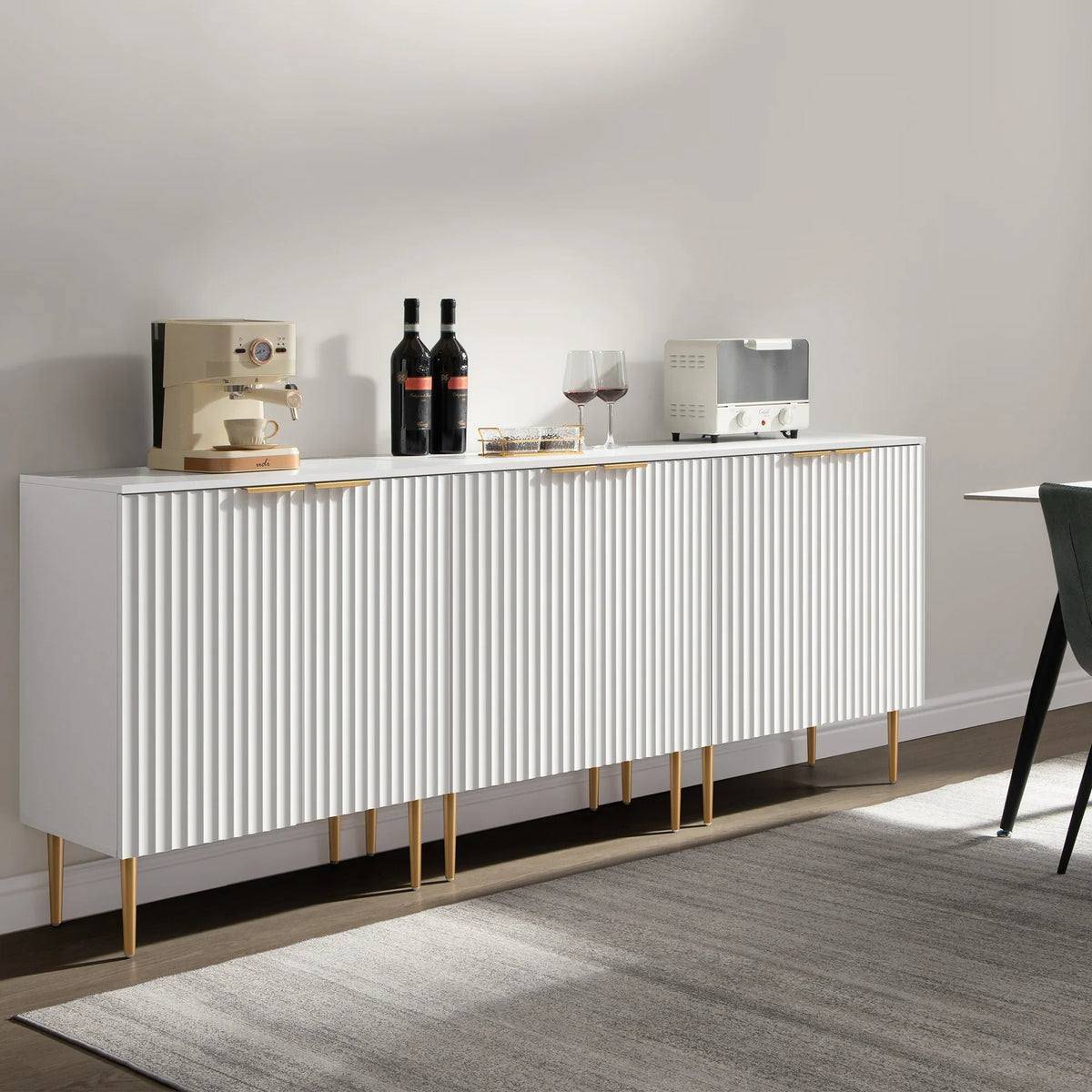 Modern white buffet cabinet with gold legs, coffee machine, wine bottles, and glasses on top