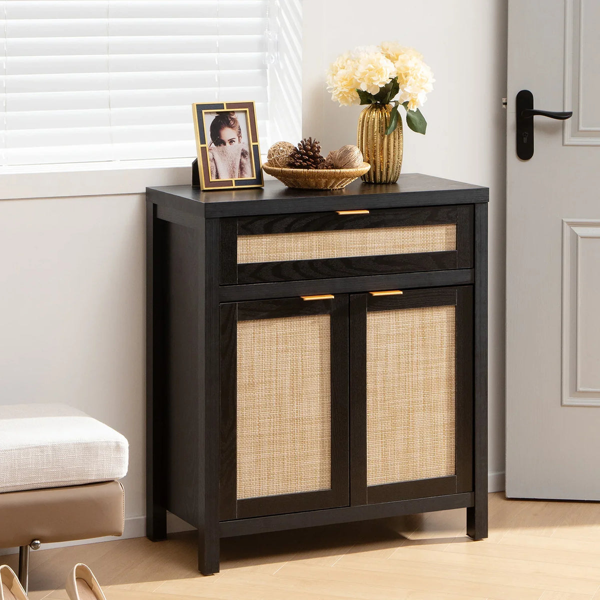 Modern black wood rattan accent cabinet in entryway, topped with flowers and photo frame