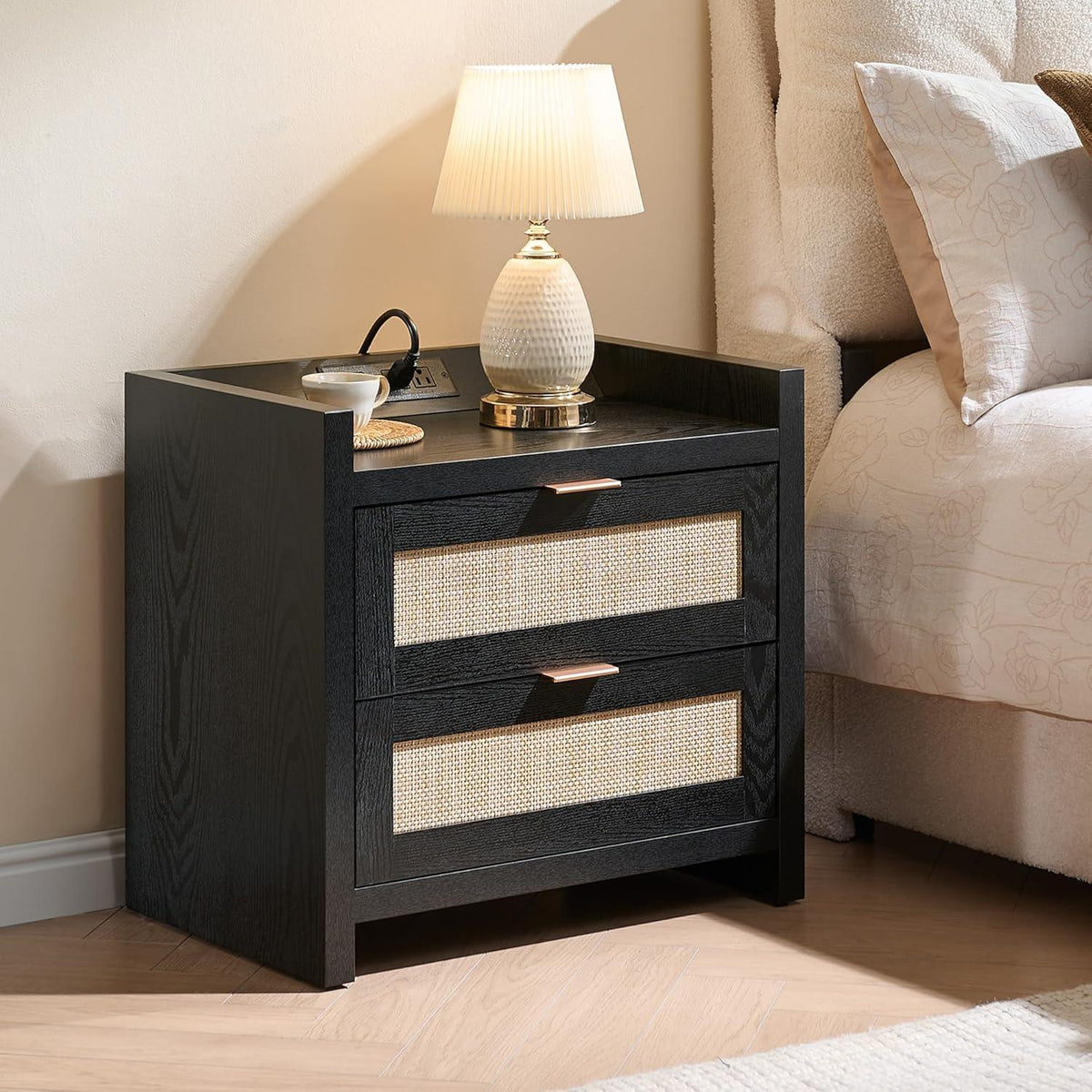 Modern black nightstand with rattan drawers, table lamp, and cup beside a bed