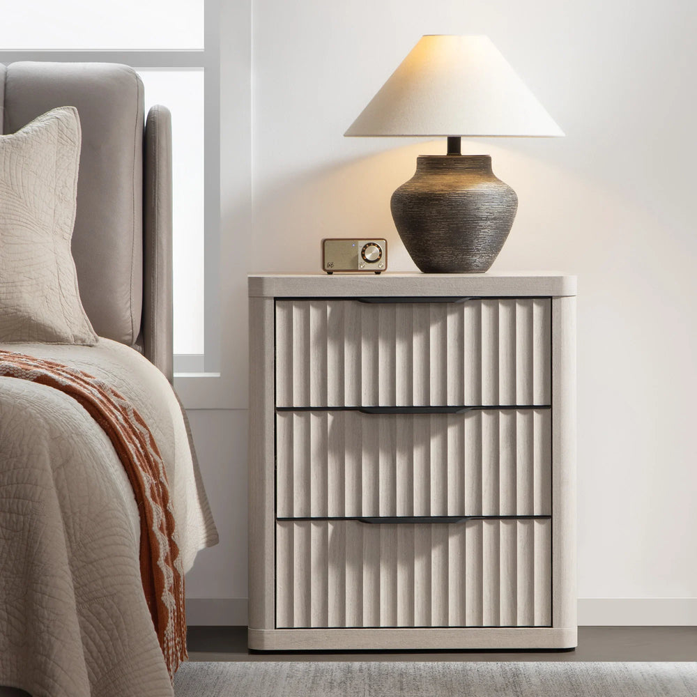 Modern bedroom with beige fluted nightstand, table lamp, vintage radio, and cozy bedding