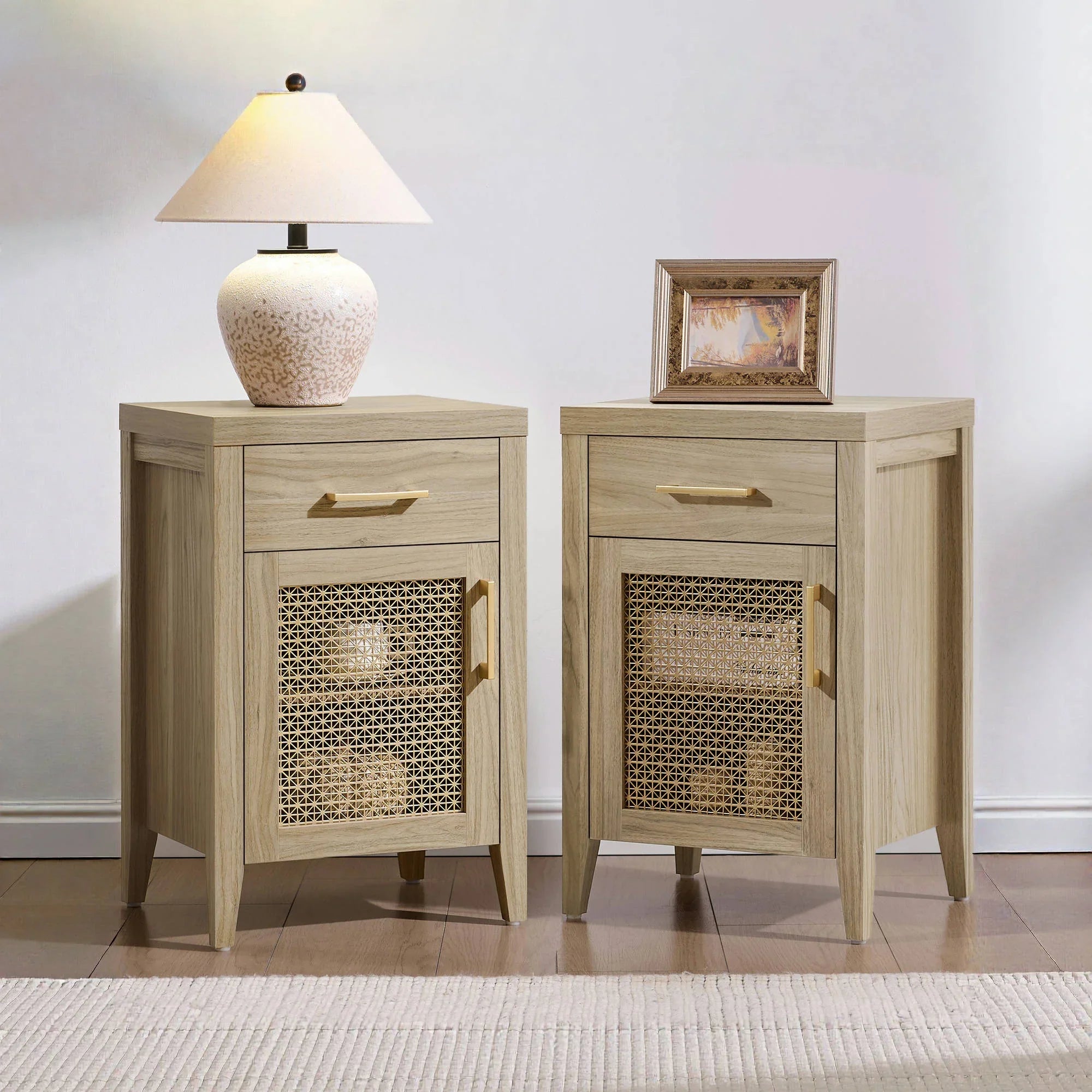 Pair of light wood nightstands with woven cane doors, lamp, and framed picture in modern bedroom.