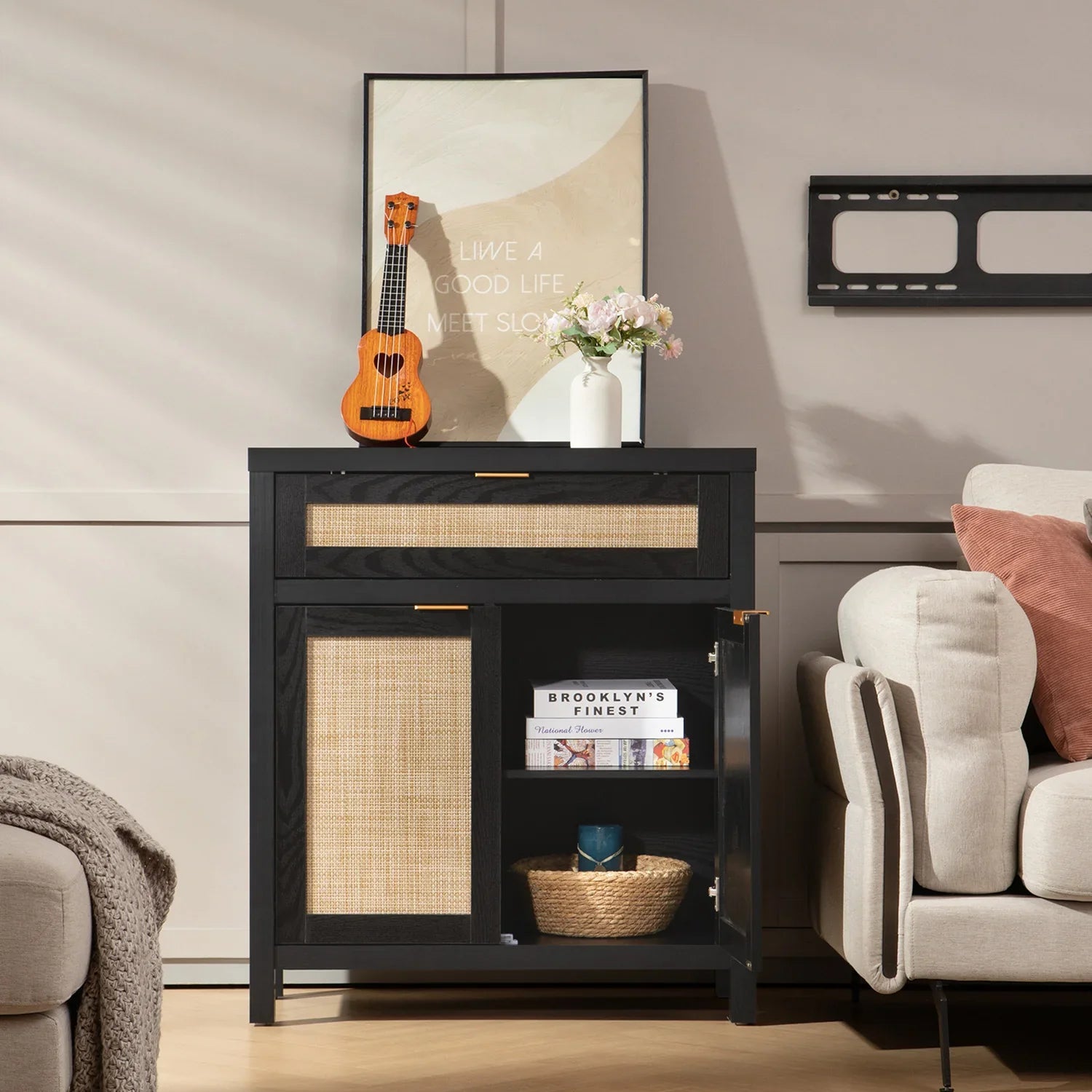 Black and rattan accent cabinet with ukulele, white vase of flowers, and modern décor in living room