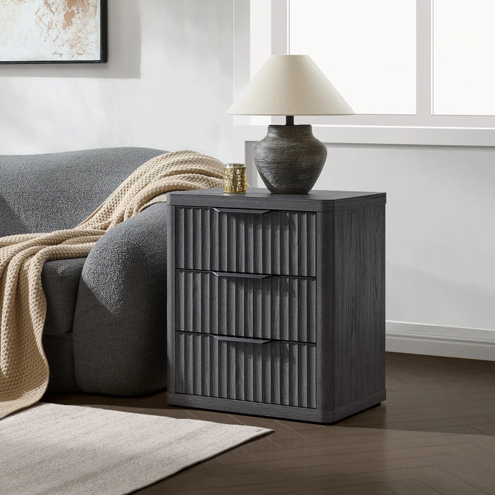 Modern dark wood nightstand with ribbed drawers, table lamp, and cozy gray sofa in living room