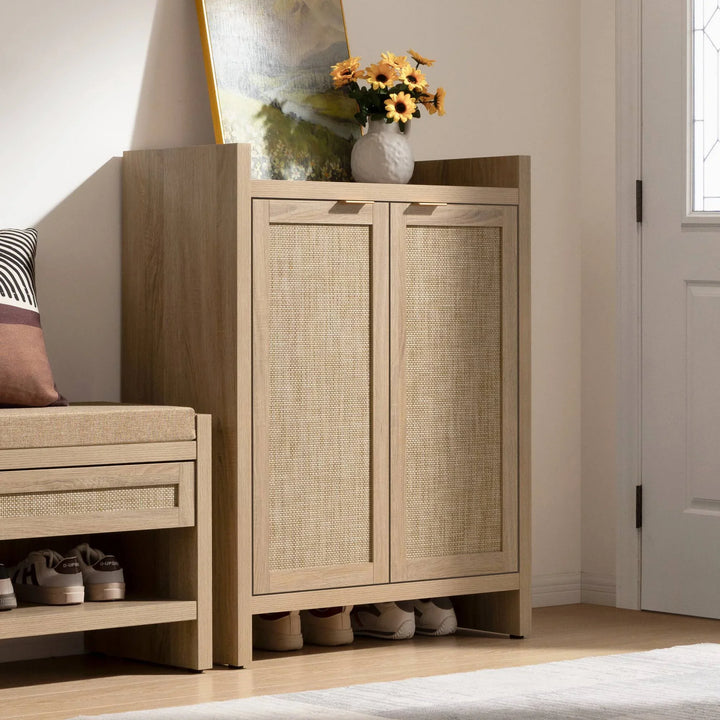 Modern oak shoe cabinet with woven rattan doors, topped with flowers and a painting in entryway
