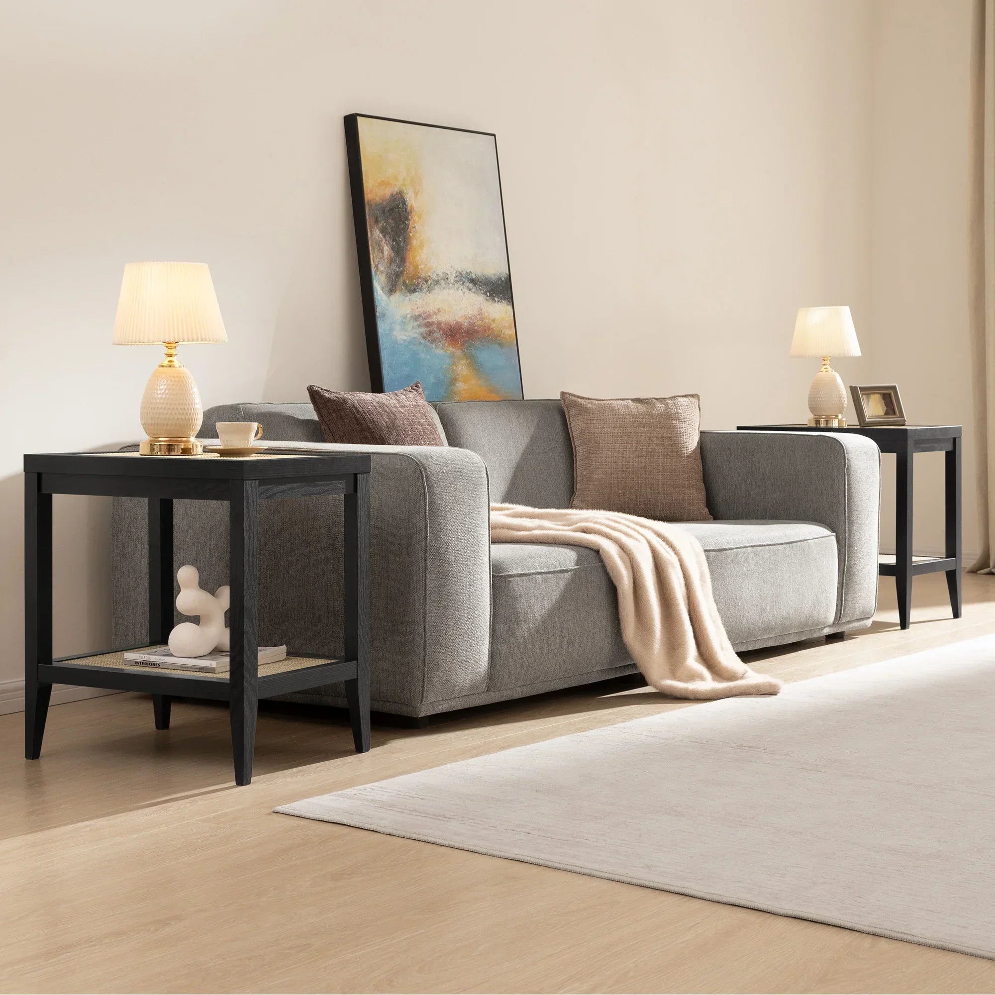 Modern living room with gray sofa, black end tables, table lamps, and abstract wall art