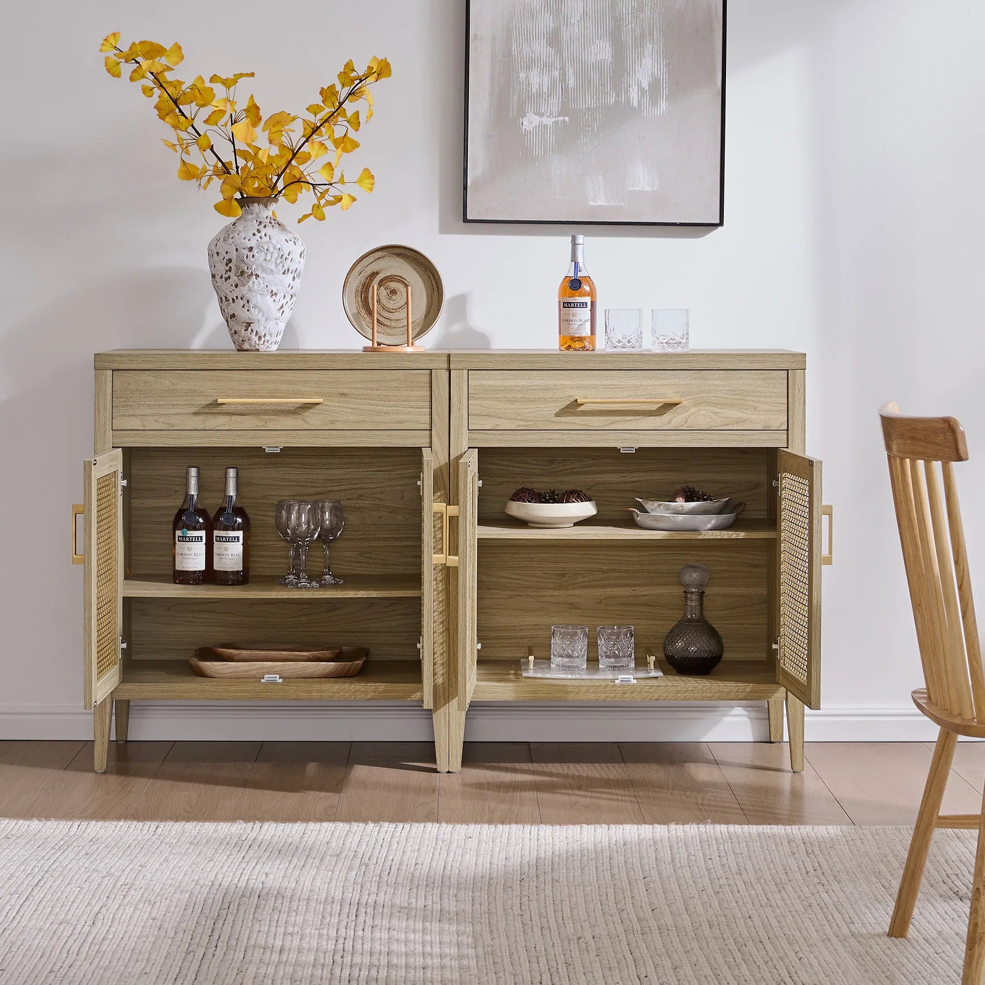 Modern light wood sideboard with open shelves, glassware, bottles, and yellow floral vase